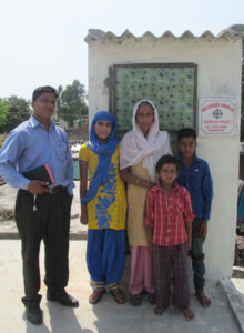 pastor and a family standing in front of an outdoor toilet