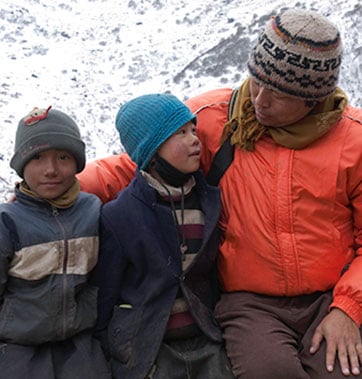 man sitting next to two boys all wrapped in winter clothing in the snow
